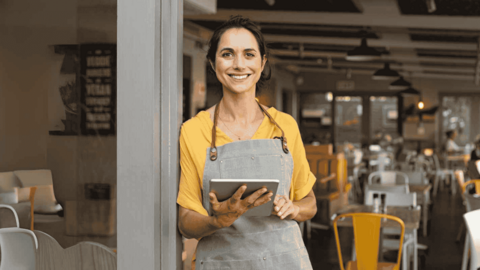 Frau steht vor ihrem Laden und hat ein iPad in der Hand 
